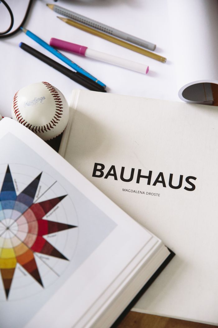 An artistic workspace featuring a Bauhaus design book, art supplies, and a baseball for inspiration.