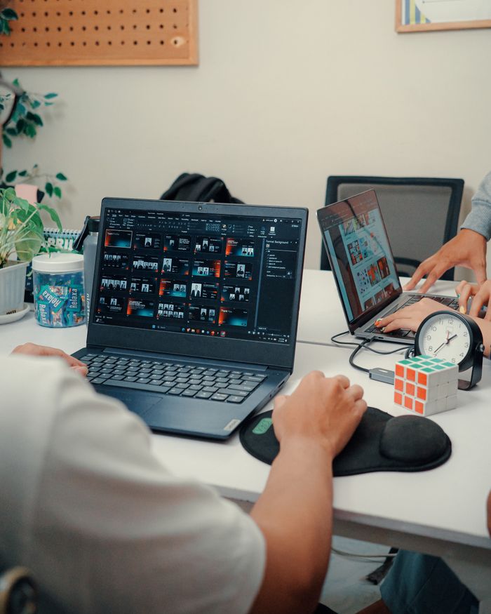 Two people working on laptops at a modern office desk with coffee and a Rubik's cube.